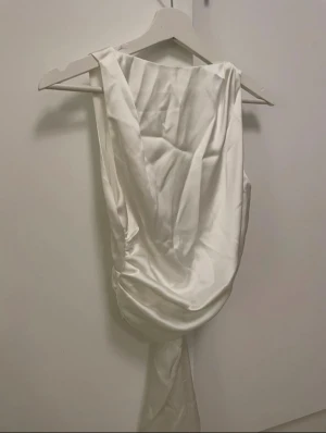 Vit topp med öppen rygg från Zara - Supersnygg vit topp med öppen rygg och knyte i ryggen från Zara i glansigt tyg. Tröjan är lite skrynklig men följs tvättrådeb går den att få som ny!