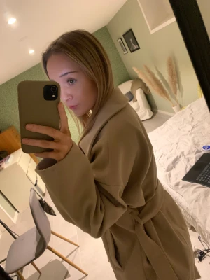 Kappa från Gina tricot - Säljer en beige kappa med bälte i midjan och stora fickor framtill. Jackan har klassisk krage, knappar och är i ett mjukt material som känns lite ulligt. Perfekt oversized passform och långa ärmar.