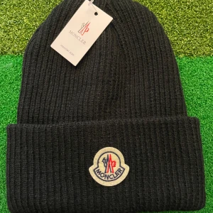 Svart ribbstickad mössa från Moncler - Svart ribbstickad mössa från Moncler med klassisk uppvikt kant och broderad logotyp framtill. Tillverkad i mjukt ullmaterial som håller dig varm och snygg under kyliga dagar. Perfekt accessoar för dig som gillar stilrena och exklusiva detaljer.