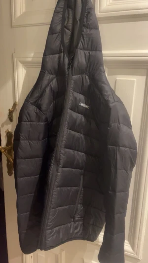 Svart pufferjacka från Jack&jones & Jones - Säljer en svart pufferjacka från Jack & Jones med huva och dragkedja. Jackan är quiltad och har två praktiska fickor med dragkedja framtill. Perfekt för kalla dagar och har en clean, stilren look.