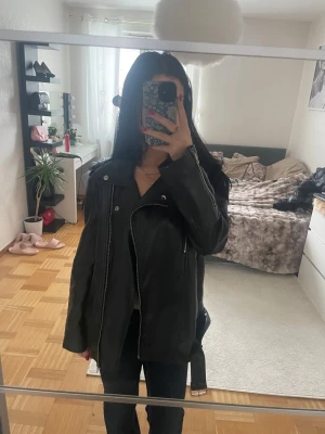 Svart skinnjacka med bälte och dragkedjor - Säljer en svart skinnjacka från shein i  bikerstil med silvrig dragkedja, knappar och bälte i midjan. En av banden till kedjan har gått av som syns på sista bilden.