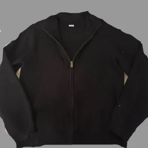 Svart stickad kofta med dragkedja - Svart stickad kofta med hel dragkedja framtill och ribbad krage. Långärmad modell som är enkel att matcha med olika outfits. Perfekt för kyliga dagar när du vill ha något stilrent och bekvämt. Stickat material 