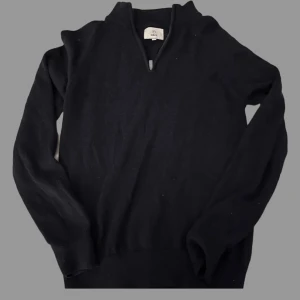 Mörkblå stickad tröja från Bläck - Snygg mörkblå stickad tröja från Bläck i storlek S. Tröjan har en half zip-dragkedja vid halsen och är långärmad med ribbade muddar. Perfekt för dig som gillar enkel och stilren design med lite sportig touch.