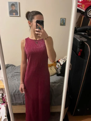 Glittrig vinröd långklänning med slits från DICE - Säljer en vinröd långklänning från DICE med glittrigt tyg. Klänningen är ärmlös och har en rak, enkel passform som sitter snyggt på kroppen. Perfekt för dig som vill sticka ut med lite extra glitter. Materialet känns mjukt och följsamt. Den har slits. Förstor för mig, jag har xs/s i klänningar men ville visa hur den satt ändå. Den ska ju passa 38/40. 