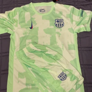 Grönvit FCB fotbollströja Nike (prisförlsag) - Säljer en grönvit fotbollströja från Nike med FCB-logga på bröstet och matchande shorts. Tröjan har korta ärmar och ett unikt mönster i grönt och vitt. Materialet är lätt och andas tack vare Nike Breathe och Dri-FIT-teknologi. Perfekt för träning eller match.
