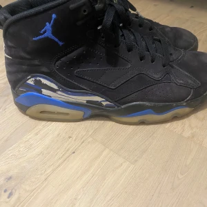 Nike Air Jordan MVP - Nike Air Jordan MVP sneakers i svart med blå detaljer och silverfärgad Nike Air-logga på hälen. Skorna har högt skaft, snörning och perforerade paneler. Sulan har blå och beige inslag, och sidan pryds av en broderad Jumpman och siffran 23. Materialet är skinn och syntet. 