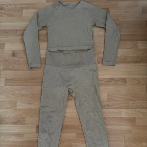 Beige ribbad croppad träningset - Säljer en beige croppad  träningset med ribbad struktur. Toppen har rund hals och är tillverkad i ett mjukt och stretchigt material som passar perfekt till gymmet eller yoga. Byxorna har hög midjan.  Enkel och stilren design som är lätt att matcha med andra träningskläder. Använd sparsam.