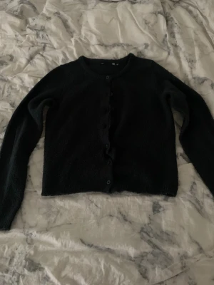 Mörkblå kofta med knappar - Mysig mörk blå kofta med rund hals och knappar hela vägen framtill. Långärmad och i ett mjukt stickat material som är perfekt för kyliga dagar. Enkel och stilren design som funkar till många olika outfits.