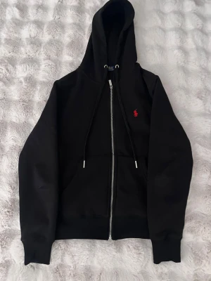 Svart hoodie från Polo Ralph Lauren - Svart hoodie från Polo Ralph Lauren med röd broderad logga på bröstet. 