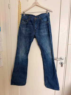 Blå bootcut jeans från Lee - Säljer ett par klassiska blå jeans från Lee med bootcut passform. Jeansen har fem fickor, snygga slitningar och Lee-logga på bakfickan samt läderpatch i midjan. Tillverkade i 100% bomull för en autentisk jeanskänsla.