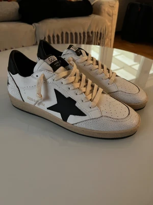 GGDB Ball Star vita sneakers med svart stjärna - Säljer ett par GGDB Ball Star sneakers i vitt skinn med svart stjärndetalj på sidan och svart häl. Skorna har aldrig använts ute utan bara testats inne, jag säljer dessa pga att jag beställde fel storlek!