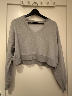 Grå croppad sweatshirt från Missguided - Grå croppad sweatshirt från Missguided med v-ringad hals och ribbade muddar. Tröjan har lång ärm och är tillverkad i mjuk bomullsmix som är perfekt för chill dagar. Enkel och stilren design som funkar till jeans eller leggings.