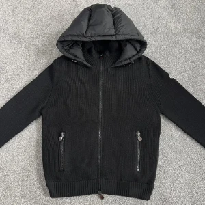 Moncler cardigan - Svart pufferjacka från Moncler med stickade ärmar och kropp i kombination med quiltad, vadderad rygg och huva. Jackan har dragkedja framtill, två fickor med dragkedja och Moncler-logga på ärmen. Perfekt för kyliga dagar med sin mix av material och stilren look.