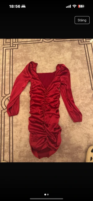 Röd sammetsklänning med puffärm - Snygg röd kort sammetsklänning med långa puffärmar och rynkade detaljer framtill. Klänningen har en djup v-ringning och markerad midja som ger en riktigt trendig siluett. Perfekt för dig som vill sticka ut med en statement-piece.