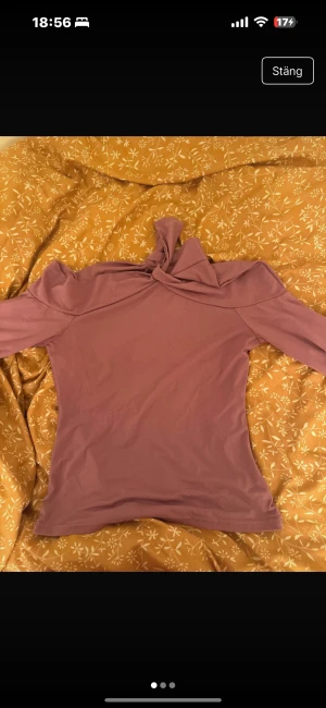 Ljuslila offshoulder topp med knut - Trendig ljuslila offshoulder topp med lång ärm och snygg knutdetalj vid halsen. Toppens material är mjukt och stretchigt, vilket gör den bekväm och smickrande. Perfekt för dig som vill sticka ut med en unik och stilren look.