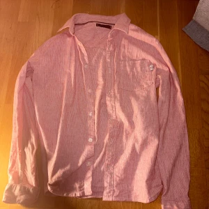 Rosa randig skjorta Tommy Hilfiger - Snygg rosa skjorta från Tommy Hilfiger med tunna vita ränder och klassisk krage. Skjortan har lång ärm, bröstficka och knappar framtill. Materialet är mjukt och består av 69% bomull och 31% linne, vilket gör den skön och luftig. Perfekt för dig som gillar stilrena detaljer.