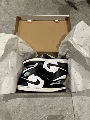 Nike Air Jordan 1 svart/vit sneakers (44) - AIR jordan (mid) i svart/vid. Skorna är i mycket bra skick utan crease-märken eller övriga skador och fläckar. De är i storlek 44 och passar killar så väl som tjejer. Till skorna följer även ett par nya crease skydd med! 