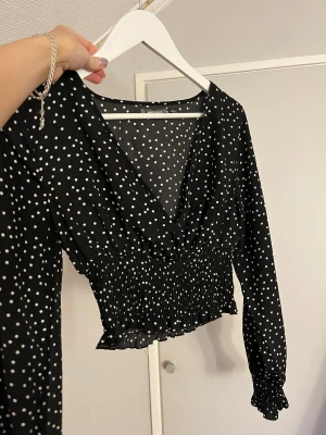 Svart prickig blus från Missguided - Säljer en svart blus från Missguided med vita prickar, v-ringad hals och tajt midja. Blusen har lite balongärmar och en lätt volangkant nedtill. Storleken är 38 men  den är mer som 36. Knappt använd 