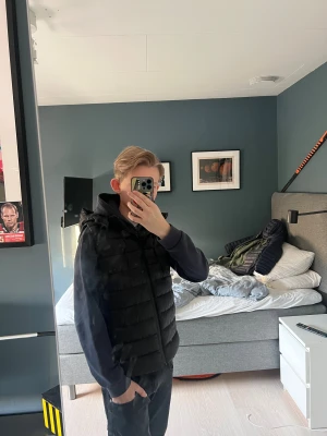 Svart dunväst - Säljer en svart dunväst med avtagbar huva och dragkedja framtill. Säljer den pga av att jag inte har använt den så mycket men en bra och snygg väst som är som ny använd typ 5 gånger pris kan diskuteras vid snabb affär hör av vid minsta lilla!