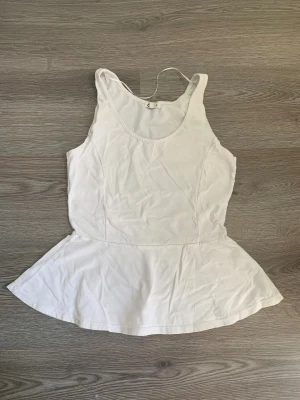 Vit peplum linnetopp från Cubus - Säljer en vit peplum linnetopp från Cubus i storlek S. Toppen är ärmlös med rund halsringning och har en utställd volang nedtill som ger en snygg siluett. Materialet känns mjukt och lätt, perfekt för varma dagar. Enkel och fräsch design som är lätt att matcha.