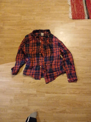 Rutig rödblå skjorta från Lee M - Snygg rutig skjorta från Lee i regular fit, storlek M. Skjortan har röda och blå rutor med vita detaljer, klassisk krage och knäppning framtill. Perfekt för en avslappnad och cool stil.