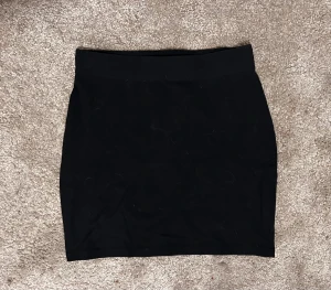 Svart tight kortkjol - Säljer en svart tight kortkjol med enkel och stilren design. Kjolen har rak form och är perfekt för dig som gillar minimalistiska plagg. Materialet känns mjukt och följsamt mot kroppen. Passar dig som vill ha en klassisk svart kjol i garderoben.