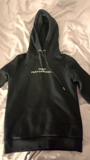 Svart hoodie Peak Performance S - Svart hoodie från Peak Performance i storlek S. Klassisk design med vit logga på bröstet, stor huva med snörning och en rymlig magficka. Använt 1 gång, säljer då jag inte använder den. Inga defekter. Bara skriva om du har nån fundering🩷 pris kan diskuteras! 
