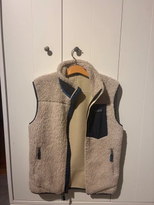 Patagonia väst - Snygg och varm Patagonia Retro-X väst i beige (stl S). Tjock sherpa-fleece med vindtätt meshfoder. Fint skick inga fel, alla dragkedjor funkar. Bröstficka + två sidofickor. Äkta produkt, taggar finns. Säljes då den inte används.