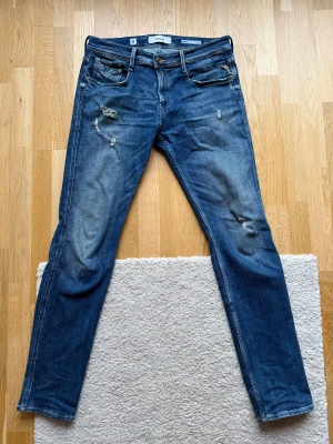 Replay Anbass blå jeans slim fit - Använda 2-3 gånger, så gott som nyskick. Snygga blå jeans från Replay, modell Anbass med slim fit. Jeansen har slitna detaljer och klassisk femficksdesign. De är tillverkade i jeansmaterial med en mörkblå tvätt. W34 L34