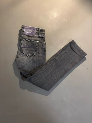 Svarta jeans från Jacob Cohen - Snygga svarta jeans från Jacob Cohen med lila detaljer och broderad logga på fickan. Klassisk femficksmodell med kontrastsömmar och en lila patch baktill. Jeansen har rak passform och är tillverkade i mjukt denimtyg för en skön känsla.