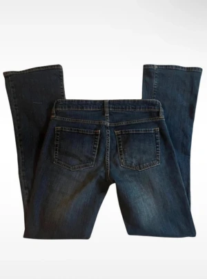 Gap vintage blå bootcut jeans - Snygga blå jeans från Gap i modellen Sexy Bootcut Fit. Klassisk femficksdesign, med medelblå tvätt och lätt slitning vid benslut. Jeansen har normal passform och är tillverkade i mjukt jeanstyg med gul kontrastsöm. Perfekt för dig som gillar bootcut och vill ha en cool look. Sitter som en 36. 