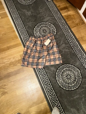   Burberry shorts - Snygga Burberry short med klassiskt rutigt mönster i beige, svart, vitt och rött. Shorten har resår i midjan och är tillverkad i ett lätt och luftigt material med meshfoder på insidan. Perfekt för dig som gillar ikoniska designerplagg.