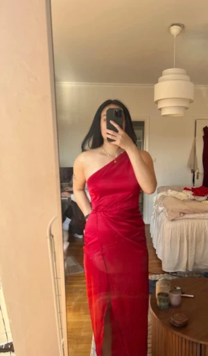 Röd one shoulder långklänning Nelly - Röd långklänning från Nelly i satinliknande material. Klänningen har one shoulder-design, markerad midja och en slits framtill. 
