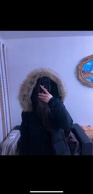 Svart pufferjacka med fuskpäls från Zara - Svart pufferjacka från Zara med stor huva kantad av beige fuskpäls. Jackan har dragkedja framtill, två sidofickor och quiltad design. Perfekt för kalla vinterdagar och har en snygg, lite oversized passform. Snygg och varm att bära när det är kallt ute. Pälsen är väldigt skönt och mjukt. 