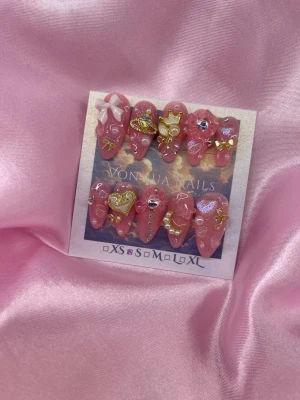 MiMi (S);Medium Almond - Set med handgjorda rosa lösnaglar i en medium mandelform, dekorerade med 3D-bågar, pärlor, hjärtan, krona och guldiga detaljer. Naglarna har glittrig finish och olika storlekar, perfekta för att skapa en unik och lyxig look.S: 15 mm, 11,5 mm, 12 mm, 11 mm, 9 mm 
