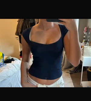 Mörkblå croppad topp med kort ärm - Säljer en mörkblå croppad topp med korta ärmar och fyrkantig halsringning. Toppen är tight och har en enkel, stilren design utan mönster eller detaljer. Perfekt att matcha med jeans eller kjol för en clean look.
