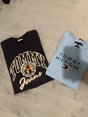 Tommy Hilfiger: 2x T-Shirt bundel pack! - Jag säljer ett bundet av 2 T-shirt som jag lagt upp för ett billigare pris   Mörkblå tröjan är i storlek M Ljusblåa är i storlek L  Båda är i bra skick, se andra annonser på min sida för mer info på varje tröja om det efterfrågas.