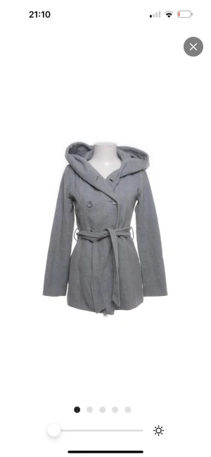 Grå kappa med huva från Amisu - Snygg grå kappa från Amisu med stor huva och bälte i midjan. Kappan har dubbelknäppning framtill och är tillverkad i en mix av polyester, ull och polyakryl. Perfekt för dig som vill ha en stilren och mysig look under vinter.