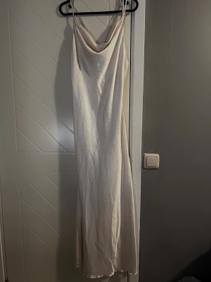  långklänning med öppen rygg - Säljer en elegant långklänning med tunna axelband och snygg draperad urringning. Klänningen har öppen rygg med korsade band och är gjord i ett glansigt, satinliknande material som ger en lyxig känsla. 