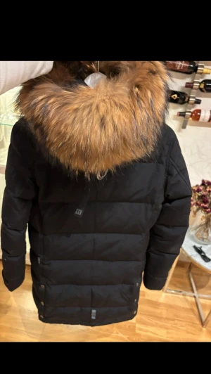 Svart pufferjacka Hollies med päls - Svart pufferjacka från Hollies med stor fluffig päls runt huvan och coolt Arctic Expedition-tryck på insidan. Jackan har långa ärmar, dragkedja och knappar i sidorna. Perfekt för kalla vinterdagar och riktigt snygg streetstil.  Snygg jacka med fuskpäls.  Använd en vinter.  Stl 40 men mer en stor 38.  Så passar både 38 och 40 storlekar.  Nypris 5100kr  Pris kan diskuteras med rätt att nekas om det är skambud. 