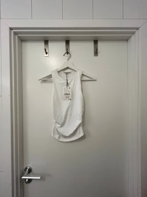 Vit linnetopp från Pull&Bear Small - Fräsch vit topp från Pull&Bear i storlek S. Modellen är ärmlös med rund hals och har snygga rynkade detaljer på sidorna så den går in tightare mot midjan. Endast provad men lappen kvar på. Liten sminkfläck som går bort vid tvätt från prov.🙌🏼