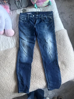 Replay blå jeans slim fit - Snygga Replay jeans i blå tvätt med slim fit och klassisk femficksdesign. Jeansen har dragkedja, knappstängning och coola slitningar på framsidan. 