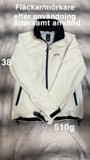 Vit vindjacka från 2848 Altitude - Snygg vit vindjacka från 2848 Altitude med marinblå detaljer och dragkedjor. Jackan har hög krage, två sidofickor med dragkedja och justerbara muddar med kardborre. Perfekt för blåsiga dagar och outdoor-aktiviteter.🌸 Sparsamt använd men finns fläckar/mörkare efter användning. Storlek 38 