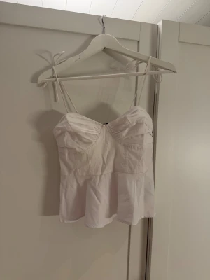 Vit linnetopp från Vero Moda - Säljer en söt vit linnetopp från Vero Moda i storlek XS. Toppen har tunna axelband, smockad rygg och en lätt volang nedtill. Framtill är den snyggt rynkad över bysten för en feminin look. Perfekt till varma dagar och enkel att matcha med jeans eller kjol.