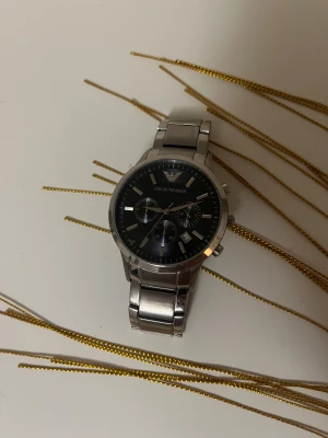 Emporio Armani silverfärgad klocka - Stilren klocka från Emporio Armani med silverfärgad länk i metall och marinblå urtavla. Klockan har kronograf-funktion, datumvisning och markerade index. Perfekt för dig som gillar klassisk design med modern touch.