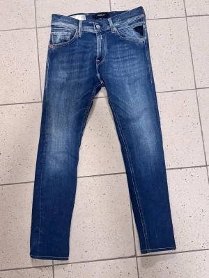 Replay jeans - Snygga Replay Jondrill jeans i blå tvätt och klassiska fem fickor. Modellen har smal passform, raka ben och detaljer på bakfickorna. Jeansen är tillverkade i stretchigt denim för extra komfort och har knappstängning framtill.