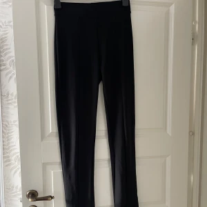 Svarta tights med slits - Svarta tights i slim fit med hög midja och smala ben. Byxorna har diskreta pressveck och en snygg slits med dragkedja vid bensluten. Perfekta för en clean och stilren look. Materialet känns mjukt och stretchigt.