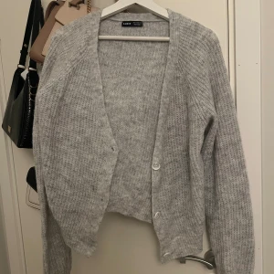 Grå stickad kofta från SHEIN - Mysig grå stickad kofta från SHEIN med lång ärm och knappar framtill. Koftan har en lätt croppad passform och är perfekt att slänga över en topp för en chill look. Enkel och stilren design som passar till det mesta.