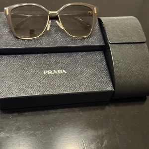 Prada solglasögon brun/guld - Snygga solglasögon från Prada med brun transparent båge och gulddetaljer. Modellen är SPR561 och har en modern, fyrkantig form. Kommer med originalfodral och box. Perfekta för dig som vill ha en lyxig och trendig accessoar. Nypris: 2899kr Säljer för: 1200kr