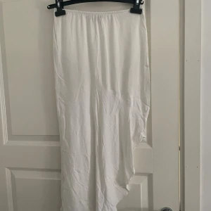 Vit långkjol med asymmetrisk slits - Säljer en vit långkjol med snygg asymmetrisk slits. Kjolen har resår i midjan och är tillverkad i ett lätt och flowy material som passar perfekt till varma dagar. Enkel och stilren design som är lätt att matcha med olika toppar 🤍